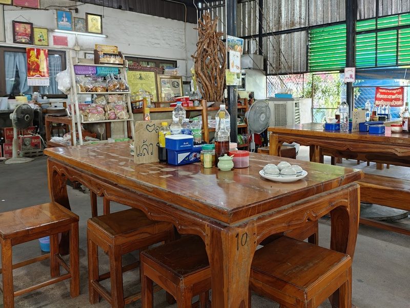 ในร้านเนื้อต้มแม่สมร โต๊ะไม้แกะขาและม้านั่งไม้ใต้หลังคาโล่ง ผนังติดรูปและชั้นวางขนม